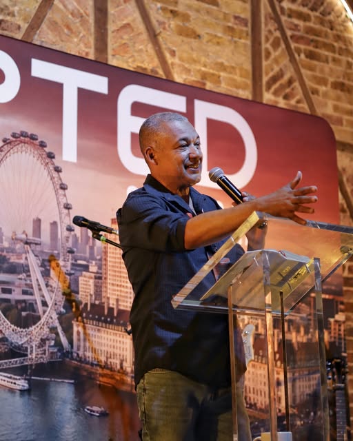 A speaker laughs mid-sentence at the lectern, the Accepted banner behind him