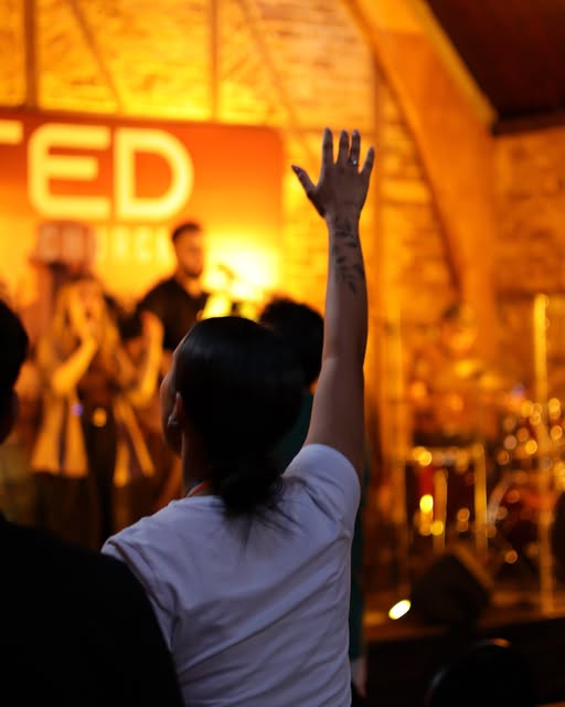 A worshipper raises a hand during a warmly lit worship set